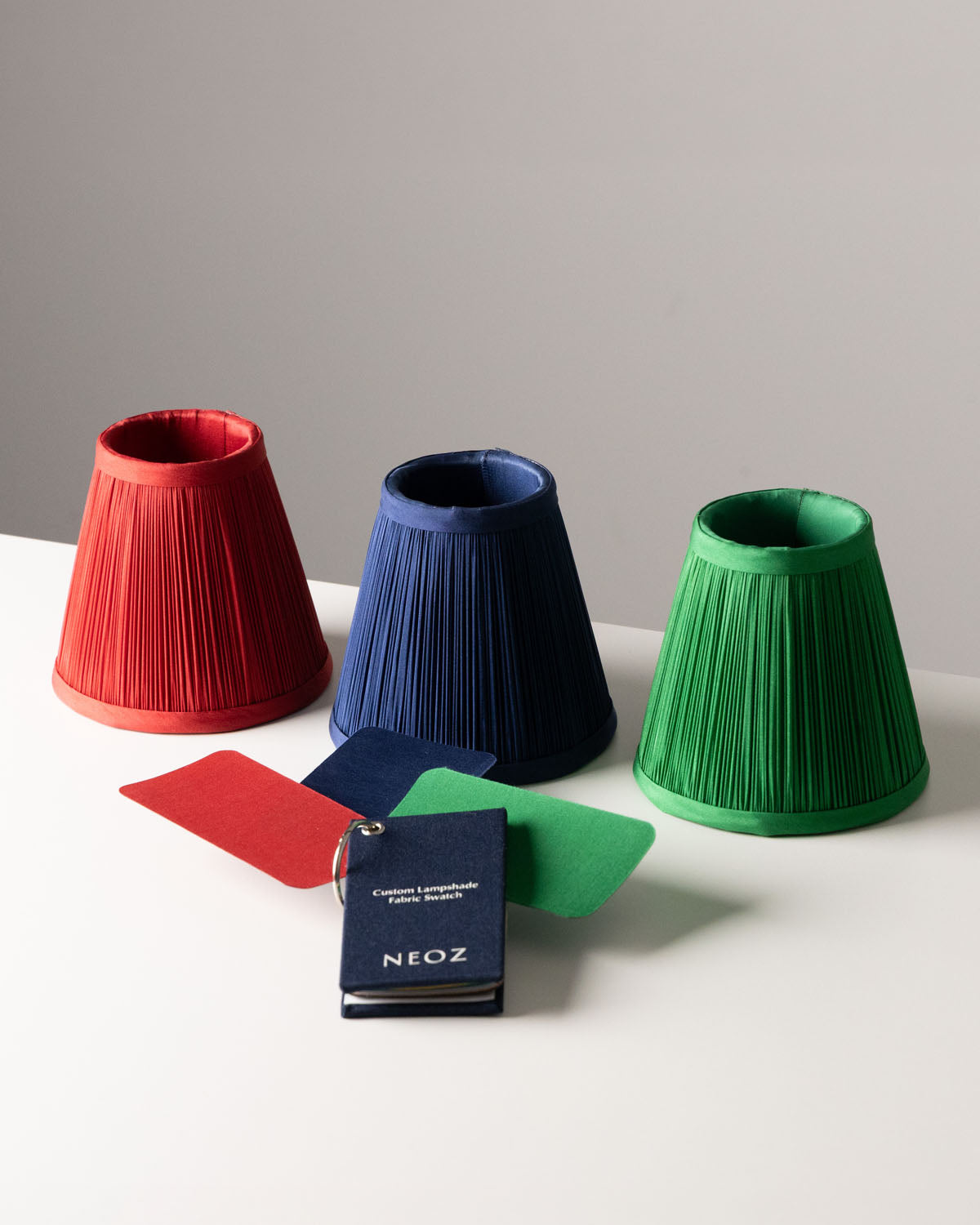 Three NEOZ custom pleated lampshades in red, navy and green matched to fabric swatches from the sample pack