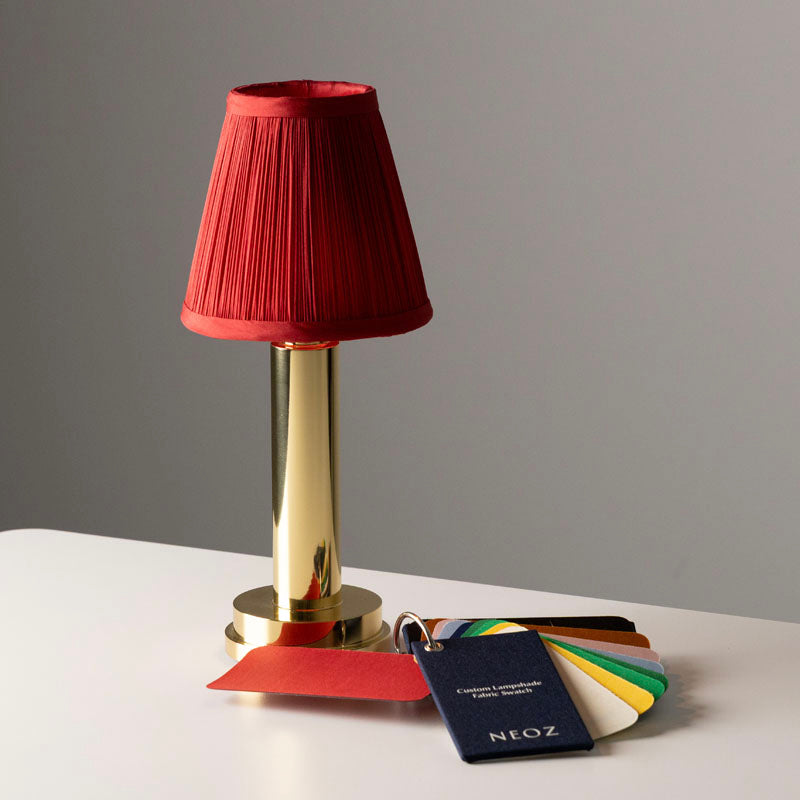 NEOZ cordless lamp with custom red pleated silk lampshade beside a fabric swatch sample pack